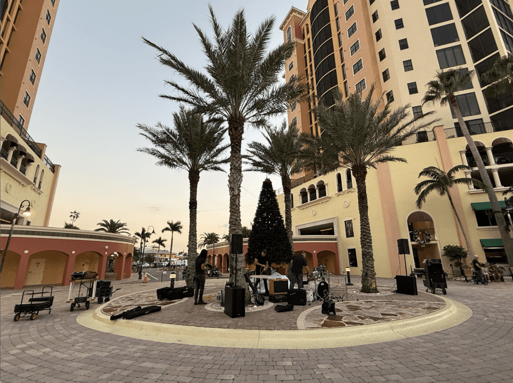 Courtyard at Harbour Marina near Fathoms Cape Coral at sunset, with palm trees, waterfront views, and live music equipment set up for an evening event.