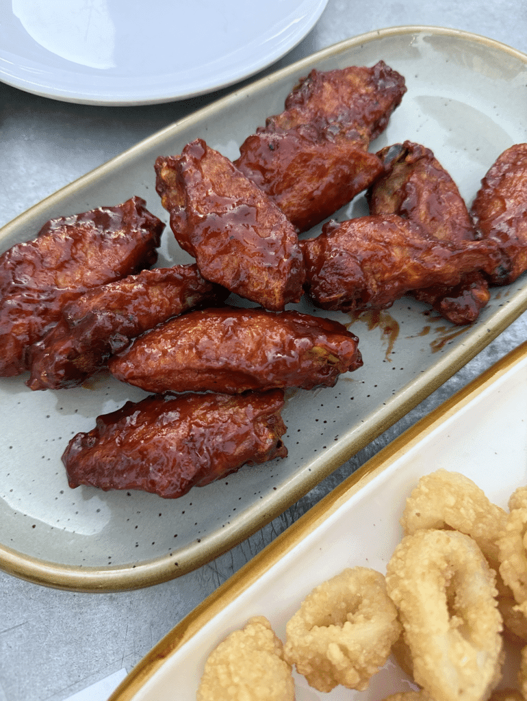House wings glazed in a dark, sticky sauce served on a platter at Fathoms Cape Coral, showcasing a popular bar appetizer.