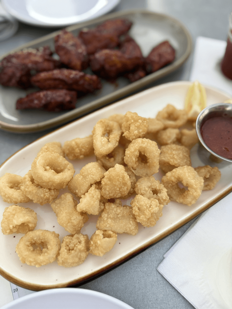Fried calamari appetizer served with marinara sauce at Fathoms Cape Coral, featuring golden crispy rings on a white platter.