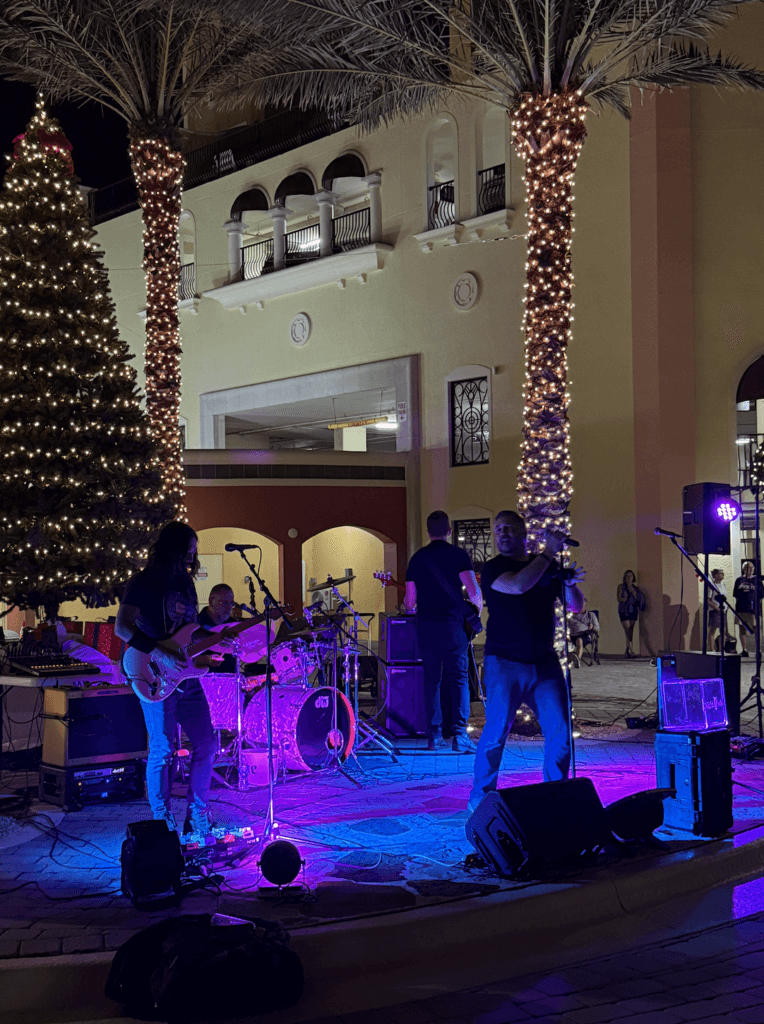 Live band performing at night in the outdoor courtyard at Fathoms Cape Coral, featuring colorful stage lighting, palm trees, and a lively waterfront atmosphere.
