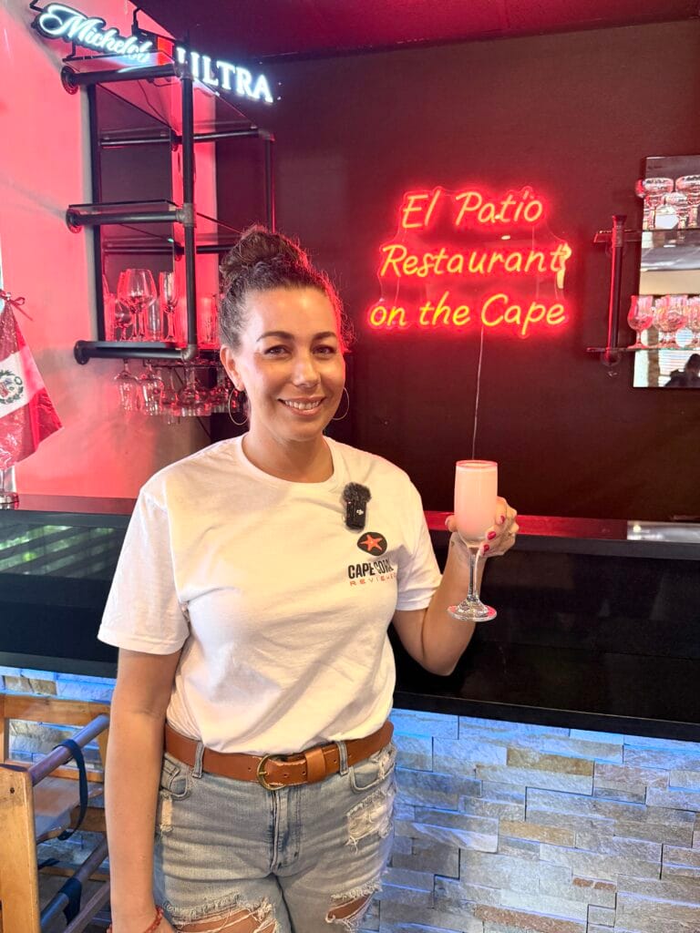 Marissa at the bar holding a Margarita with El Patio Peruvian Restaurant sign in the background in Cape Coral.