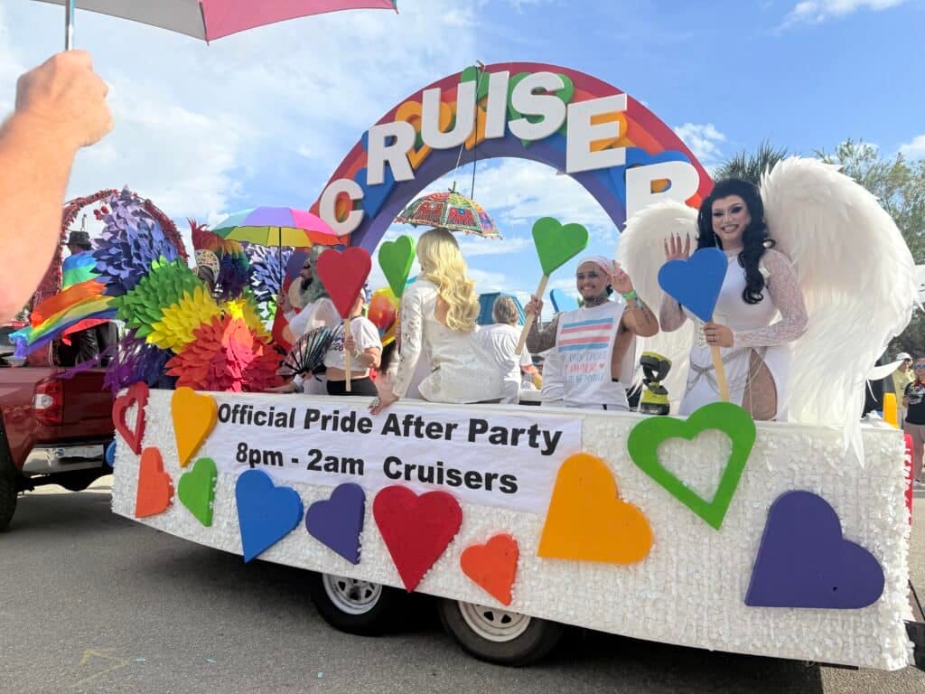 Participants waving from a decorated float during the Cape Coral pride festival parade with rainbow colors and heart decorations.