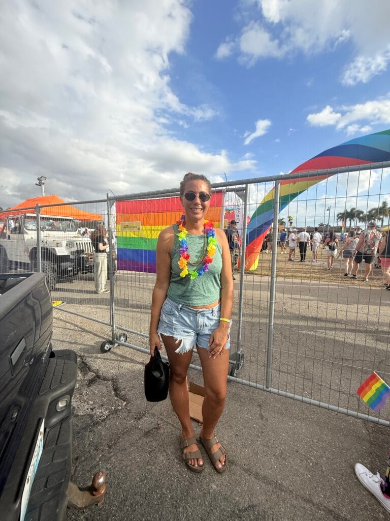 Festival attendee posing near rainbow flags at the Cape Coral pride festival grounds on a sunny day.