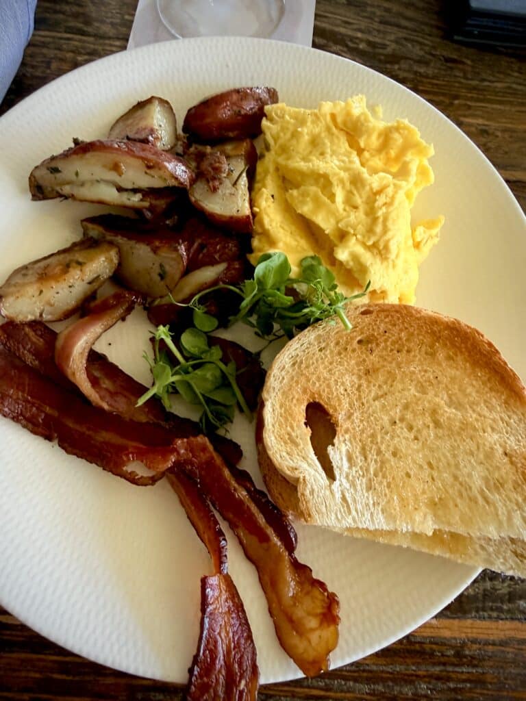 Farm-to-table breakfast plate with eggs, crispy bacon, potatoes, toast, and fresh greens at Blossom & Brie brunch.