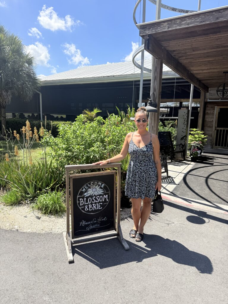 Woman posing by Blossom & Brie sign, a popular farm-to-table dining and weekend brunch destination in North Fort Myers.