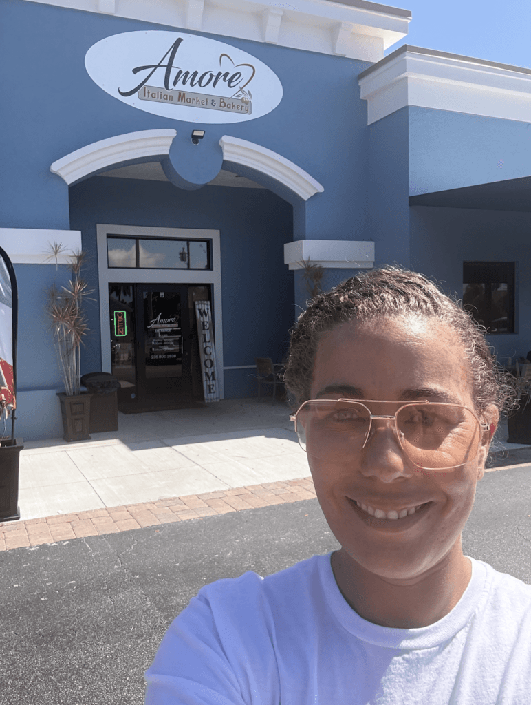 Amore Italian Market And Bakery storefront in Cape Coral with customer smiling outside the entrance.